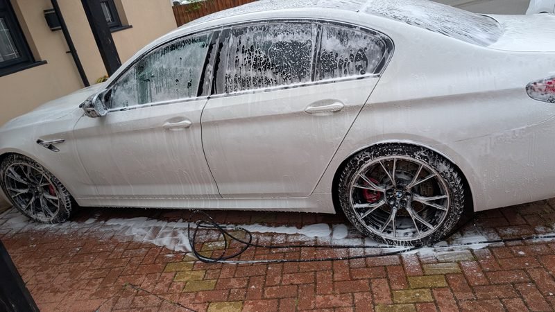 White BMW M5 covered in snow foam on a residential driveway during a professional mobile valet