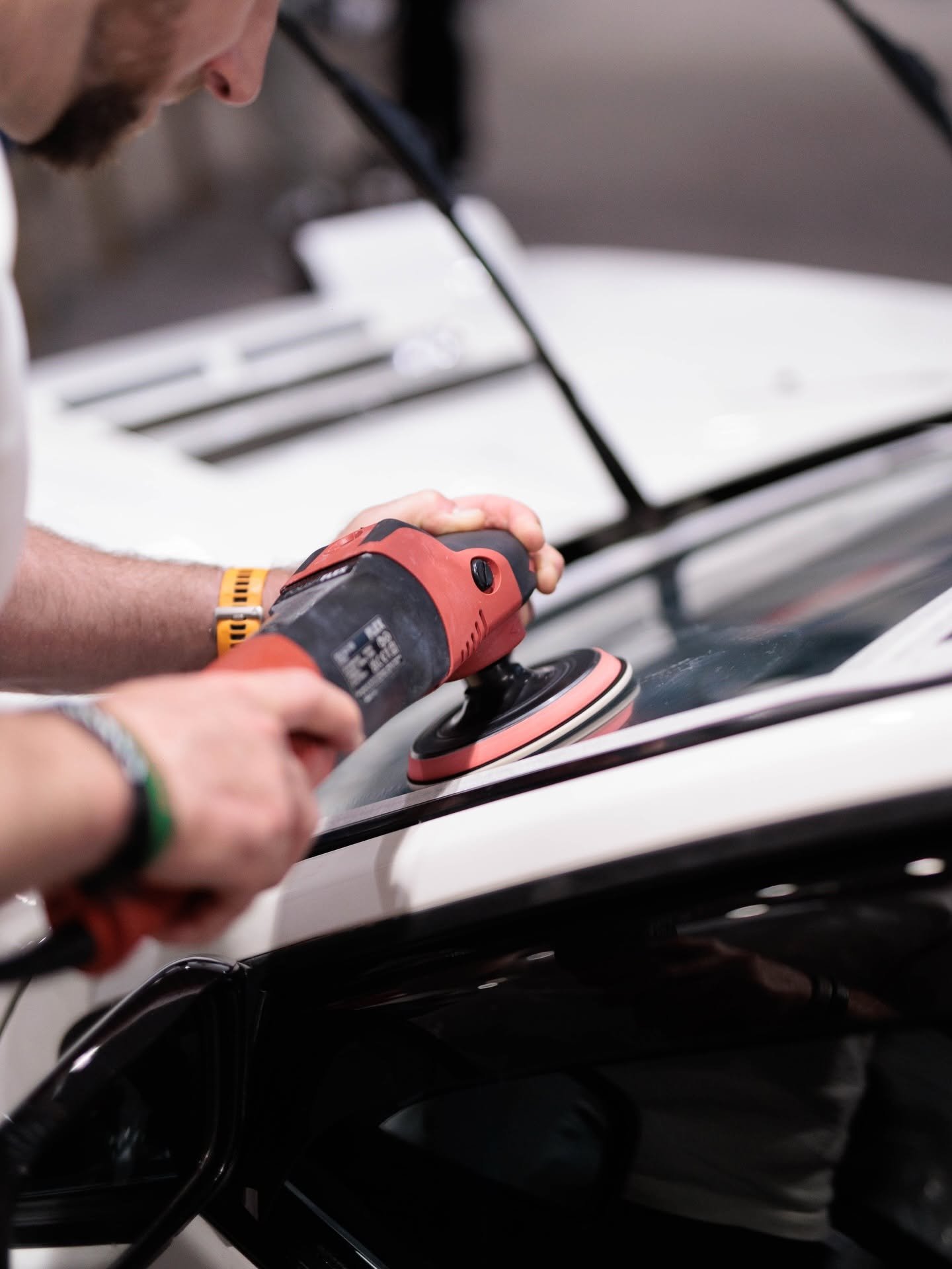 Professional using a dual-action machine polisher to carry out paint correction on a car bonnet