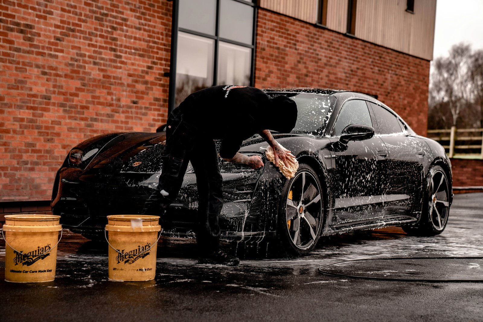 Professional hand car wash using two bucket method on a black Porsche